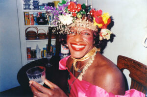 Drag queen and LGBTQ+ activist Marsha P Johnson holding a drink and smiling at the camera. 