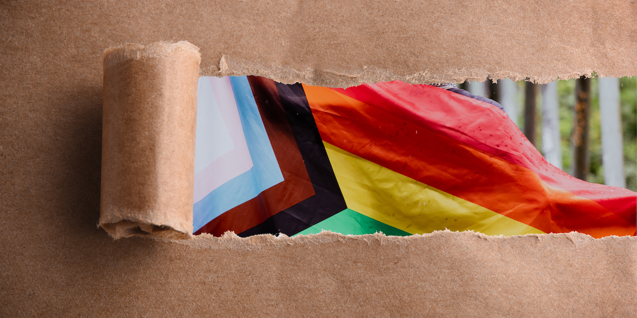 Brown paper torn artistically to reveal the pride flag underneath.